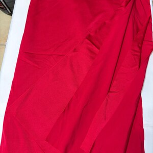 May include: A vibrant red fabric with a smooth, slightly reflective surface texture. The material is draped in a way that creates soft, flowing folds and layers, showcasing the consistent, solid red color across the entire visible surface area.