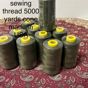 Könnte beinhalten: Olivgrüne Nähgarnkonen mit gelben Oberteilen. Der Text auf dem Bild lautet "Olive color sewing thread 5000 yards cone made in USA."