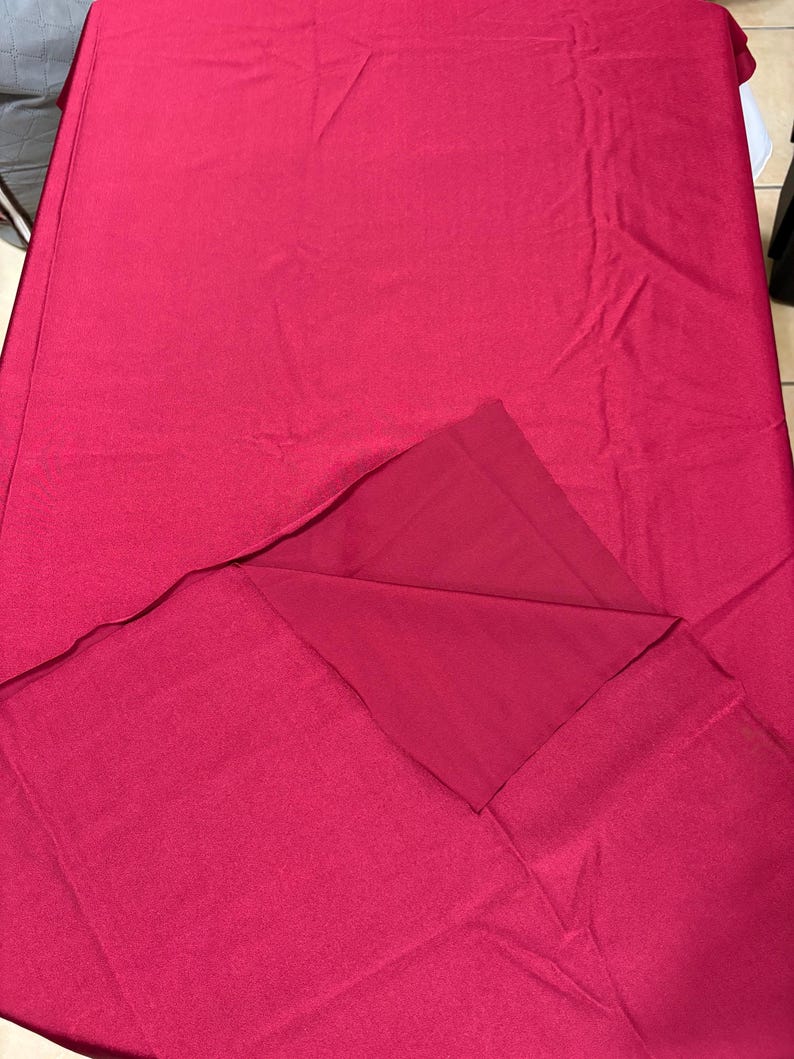 May include: A solid magenta rectangular fabric piece with a smooth, matte texture. The material is folded over at one corner, revealing a consistent deep pink color on both the front and back sides of the textile. The fabric appears flat and even.