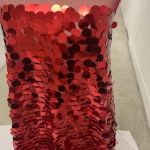 May include: Red sequin fabric with a shiny finish. The sequins are arranged in a scale-like pattern.