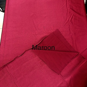 May include: A solid maroon fabric tablecloth with a smooth texture. The fabric is folded over at the corner to reveal the underside, and the word Maroon is printed in black text on the surface of the fabric in the center of the image.