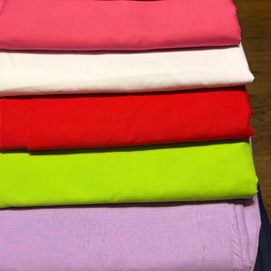 Peut inclure: Une pile de tissus pliés de différentes couleurs, notamment rose clair, bleu, rose vif, blanc, rouge, vert citron et lavande. Les tissus sont soigneusement disposés, présentant un spectre de teintes.