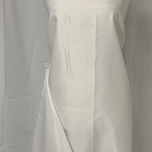 May include: A white fabric draped over a mannequin. The fabric is smooth and appears to be a lightweight material, possibly satin or silk. The fabric is gathered at the top and falls in soft folds.