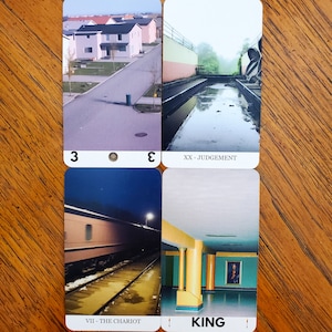 Four more cards from the liminal space tarot deck on a wooden table. On the top left is the Three of Pentacles, top right is Judgement, bottom left is The Chariot, and bottom right is the King of Wands.