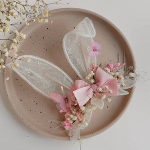 May include: A delicate hair clip featuring a pink bow, white tulle wings, and dried flowers. The clip is perfect for adding a touch of whimsy to any hairstyle.