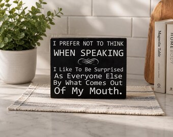 May include: A rectangular black wooden sign with white text that reads: I PREFER NOT TO THINK WHEN SPEAKING I Like To Be Surprised As Everyone Else By What Comes Out Of My Mouth. The sign features a small decorative flourish between the first two lines.