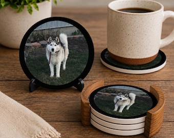 May include: A set of round drink coasters featuring a photographic print of a grey and white husky dog standing on grass. The coasters are displayed in a wooden holder and on a black stand, with one coaster placed under a speckled ceramic mug.
