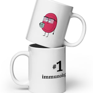 May include: Two white ceramic mugs stacked on top of each other. The top mug features a cartoon cell character wearing glasses and holding a small card that says "#1 CELL". The bottom mug has the text "#1 immunolog".