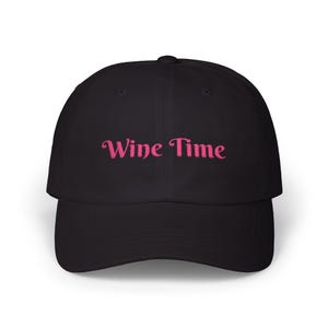 Könnte beinhalten: Schwarze Baseballkappe mit dem gestickten Text "Wine Time" in Rosa. Die Kappe hat einen gebogenen Schirm und eine strukturierte Krone, ideal für den Alltag.