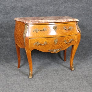 May include: A French style, two-drawer chest with a marble top. The chest is made of wood with a marquetry design and has ornate brass hardware. The chest is on a light gray background.
