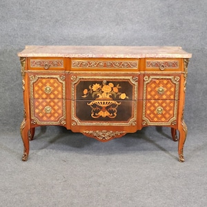 May include: A French-style dresser with a marbled top and intricate marquetry details. The dresser has three drawers with brass hardware and a floral design on the center drawer.