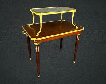 May include: A two-tiered wooden table with a glass top on the upper tier. The table has a dark wood finish and gold accents. The table is on a dark gray background.