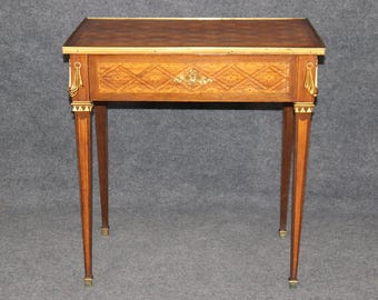 May include: A small, wooden table with a marquetry top and brass accents. The table has a single drawer and four legs.
