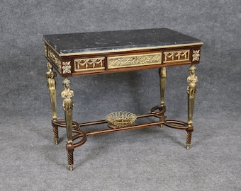May include: A dark wood table with a black marble top and ornate gold accents. The table has four legs with carved female figures and a lower shelf.