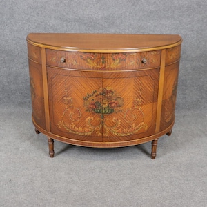 May include: A half-round wooden cabinet with a painted floral design and a single drawer. The cabinet has a dark brown finish and stands on four turned legs.
