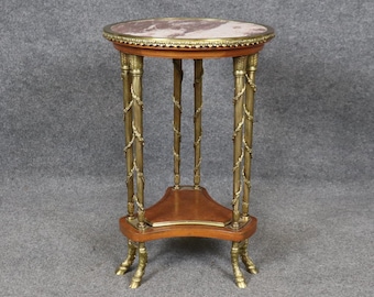 May include: A round, marble-top side table with a gold-tone, ornate base. The table has three legs with claw feet and a lower shelf.