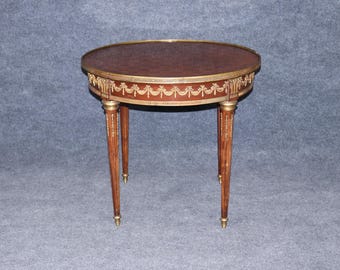 May include: A small, round antique table with a dark brown tabletop and ornate gold trim. The table has four slender, tapered legs with gold accents. The table is approximately 24 inches in diameter and 28 inches tall.