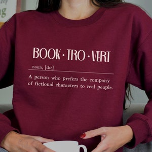 May include: Burgundy sweatshirt with white text that reads "BOOK. TRO. VERT noun, [the] A person who prefers the company of fictional characters to real people."