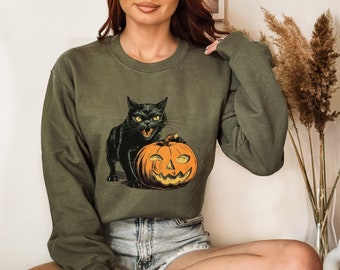 May include: A green sweatshirt featuring a black cat and a jack-o'-lantern graphic. The cat is holding the pumpkin in its paws.