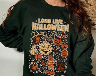 Puede incluir: Sudadera verde oscuro con un gráfico colorido de Halloween. El gráfico incluye una bruja, calabazas, fantasmas, un gato negro y el texto "LONG LIVE HALLOWEEN" y "OCT 31".