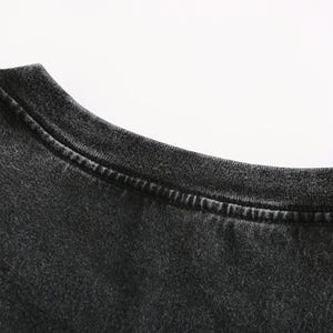 May include: Close-up of a dark gray t-shirt neckline. The fabric has a slightly faded appearance, with visible stitching along the collar. The shirt appears to be made of a soft, comfortable material.