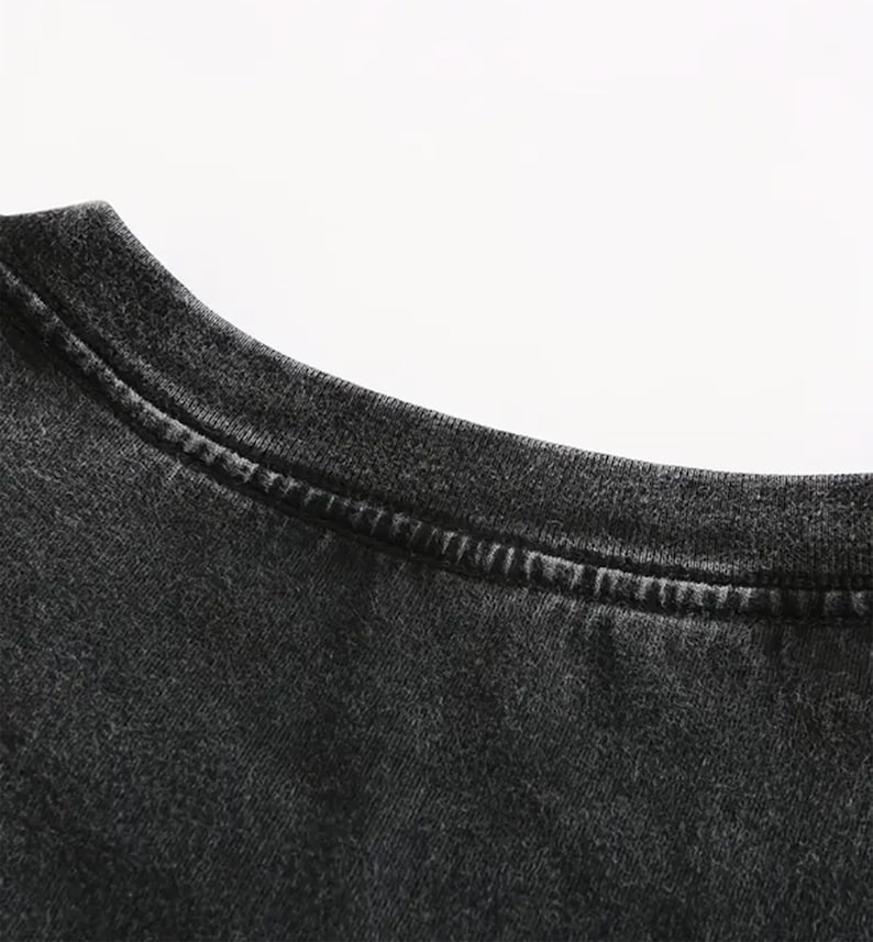 May include: Close-up of a dark gray t-shirt neckline. The fabric has a slightly faded appearance, with visible stitching along the collar. The shirt appears to be made of a soft, comfortable material.