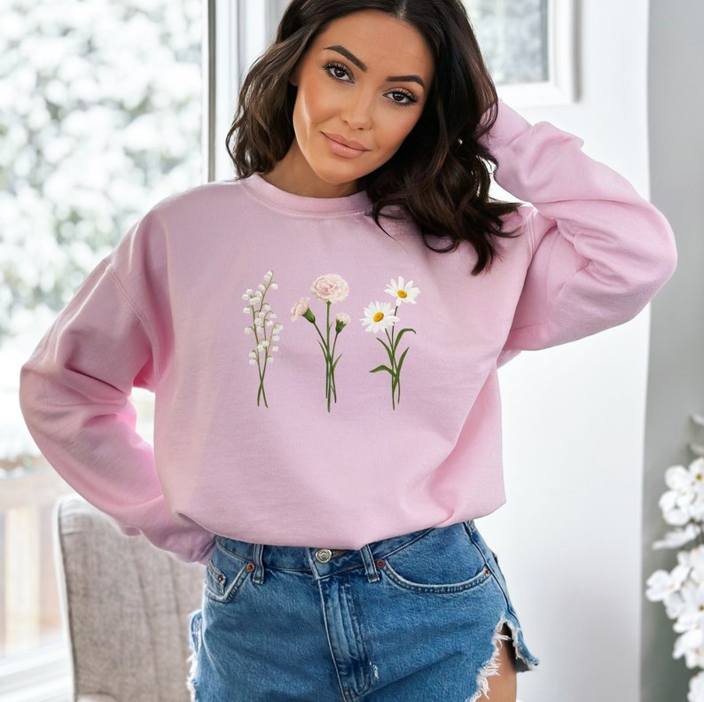 May include: A pink sweatshirt with a floral design featuring white lilies, pink carnations, and white daisies.