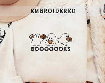 Puede incluir: Sudadera de color crema con la palabra "EMBROIDERED" en la parte superior. Debajo, tres fantasmas de dibujos animados bordados, cada uno sosteniendo libros. La palabra "BOOOOOOKS" está bordada debajo de los fantasmas.