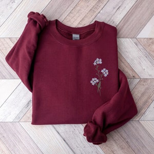 May include: Burgundy sweatshirt with a small embroidered floral design in shades of blue and green.