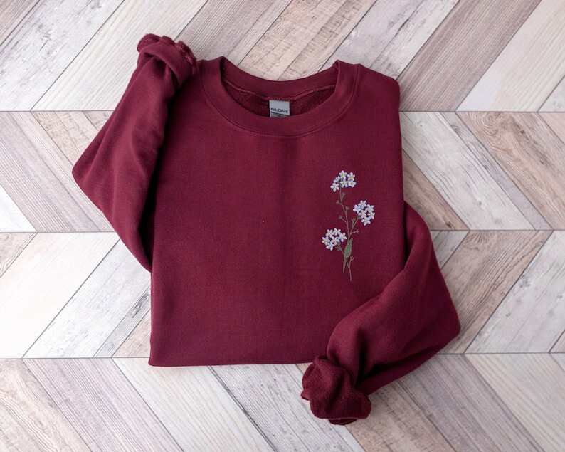 May include: Burgundy sweatshirt with a small embroidered floral design in shades of blue and green.