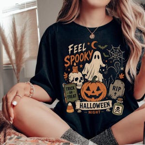 Peut inclure: Un t-shirt noir avec une impression graphique portant le texte "FEEL SPOOKY" et "HALLOWEEN NIGHT". Le motif comprend un fantôme, un chat noir, une citrouille, un crâne avec une bougie, une pierre tombale "RIP", une potion et un bonbon.