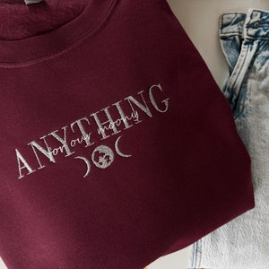 Könnte beinhalten: Burgunderfarbener Sweatshirt mit dem Text "ANYTHING for our moony" in weißer Stickerei. Die Stickerei enthält auch einen Halbmond und einen Stern.
