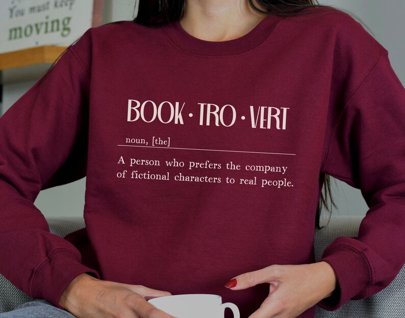 May include: Burgundy sweatshirt with white text that reads "BOOK. TRO. VERT noun, [the] A person who prefers the company of fictional characters to real people."