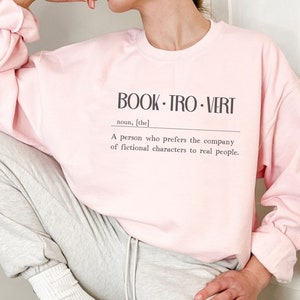 May include: A pink sweatshirt with the text "BOOK-TRO-VERT" and a definition: "A person who prefers the company of fictional characters to real people."