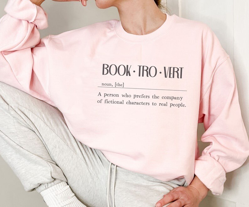May include: A pink sweatshirt with the text "BOOK-TRO-VERT" and a definition: "A person who prefers the company of fictional characters to real people."