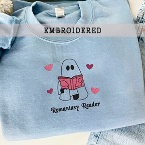 May include: Light blue sweatshirt with an embroidered design of a ghost reading a book with the text "Romantasy Reader" and pink hearts.