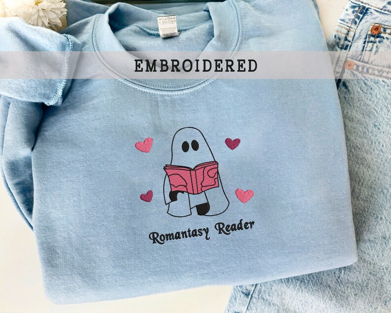 May include: Light blue sweatshirt with an embroidered design of a ghost reading a book with the text "Romantasy Reader" and pink hearts.
