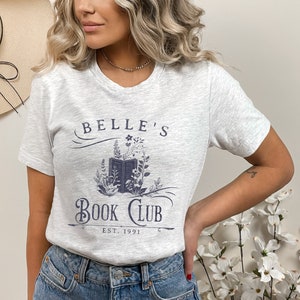 May include: A grey t-shirt with a blue graphic design that says "Belle's Book Club Est. 1991". The graphic features a book with flowers around it.