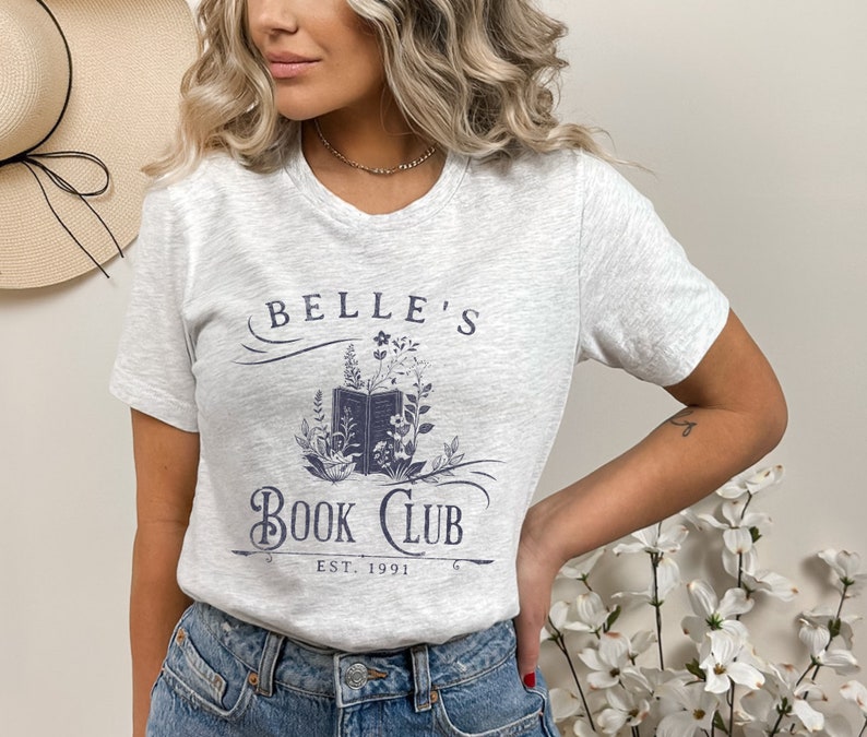 May include: A grey t-shirt with a blue graphic design that says "Belle's Book Club Est. 1991". The graphic features a book with flowers around it.