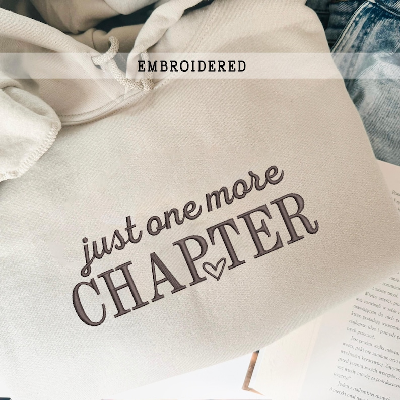 Pode incluir: Moletom bordado creme com o texto "just one more CHAPTER" em uma fonte de script marrom escuro. A palavra "EMBROIDERED" &eacute; impressa em um ret&acirc;ngulo branco. Um s&iacute;mbolo de cora&ccedil;&atilde;o est&aacute; entre as palavras "CHAPTER".