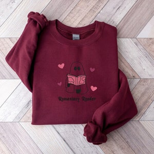 May include: Burgundy sweatshirt with a ghost reading a book and the text "Romaniacsy Reader".