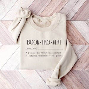 May include: A beige sweatshirt with the text "BOOK TRO VERT" and the definition: "A person who prefers the company of fictional characters to real people."