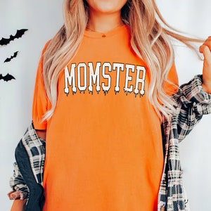 May include: Orange t-shirt with the text "MOMSTER" in white dripping letters.