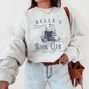 May include: A grey sweatshirt with the text "Belle's Book Club Est. 1991" and a graphic of an open book with flowers.