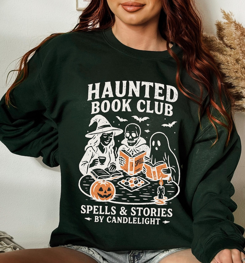 May include: Dark green sweatshirt with a white graphic that reads "HAUNTED BOOK CLUB" above illustrations of a witch, skull, and ghost reading books. The graphic also includes a jack-o'-lantern, bats, and the text "SPELLS & STORIES BY CANDLELIGHT."