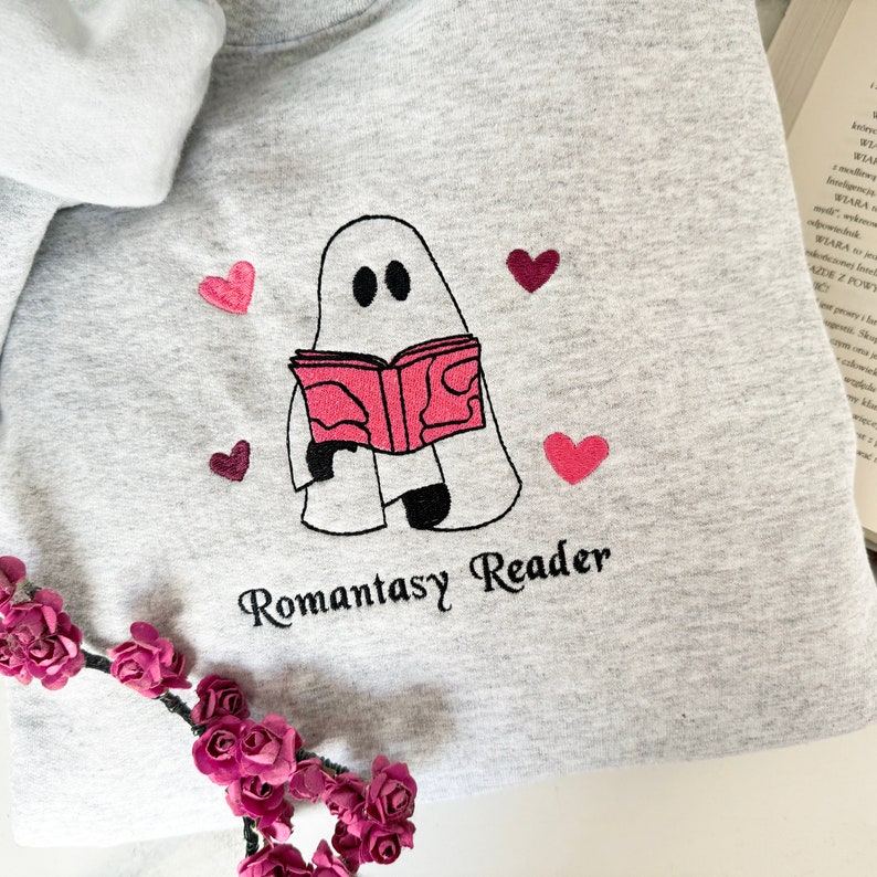 May include: A gray sweatshirt with a white ghost holding a pink book and the text "Romantasy Reader". The ghost is surrounded by pink hearts.