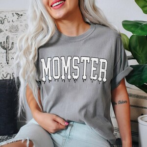 May include: A gray t-shirt with the word "MOMSTER" printed in white with a dripping effect.