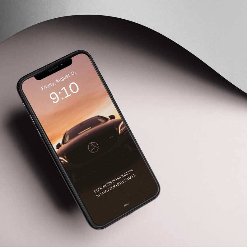 K&ouml;nnte beinhalten: Ein schwarzes Smartphone mit einem dunkelbraunen Hintergrundbild eines Autos. Die Uhrzeit ist 9:10 Uhr und das Datum ist Freitag, der 15. August. Der Text auf dem Bildschirm lautet "PROGRESS IS PROGRESS NO MATTER HOW SMALL."