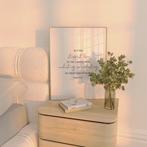 May include: A framed print with a white background and black text. The text reads "But the steadfast love of the Lord is from everlasting to everlasting on those who fear him. Psalm 103:17". The print is sitting on a wooden nightstand with a stack of books and a vase with green leaves.