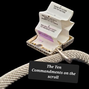 May include: A silver-toned metal locket pendant attached to a textured mesh chain. The locket is open, revealing a white accordion-folded paper scroll printed with black text, including the phrases Honor Thy Father and Thy Mother.
